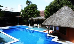 A swimming pool with a thatched-roof hut and a view of tall buildings in the background.