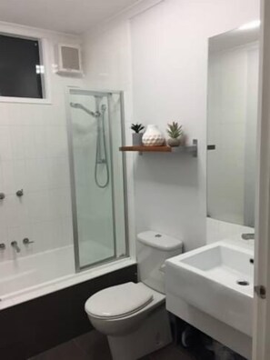 Een moderne badkamer met een douchecabine van glas, een toilet en een wastafel.
