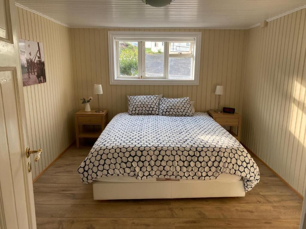 A bedroom with a bed, two bedside tables, a window, and a door.