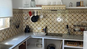 A kitchen with a granite countertop, hanging pots, a coffee machine, and a tiled backsplash. - Cozy Apartment with Stunning Sea Views, One Minute Walk from the Beach (Praia da Luz, Lagos)