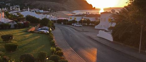 A coastal street with houses, a road, and a hill in the background.