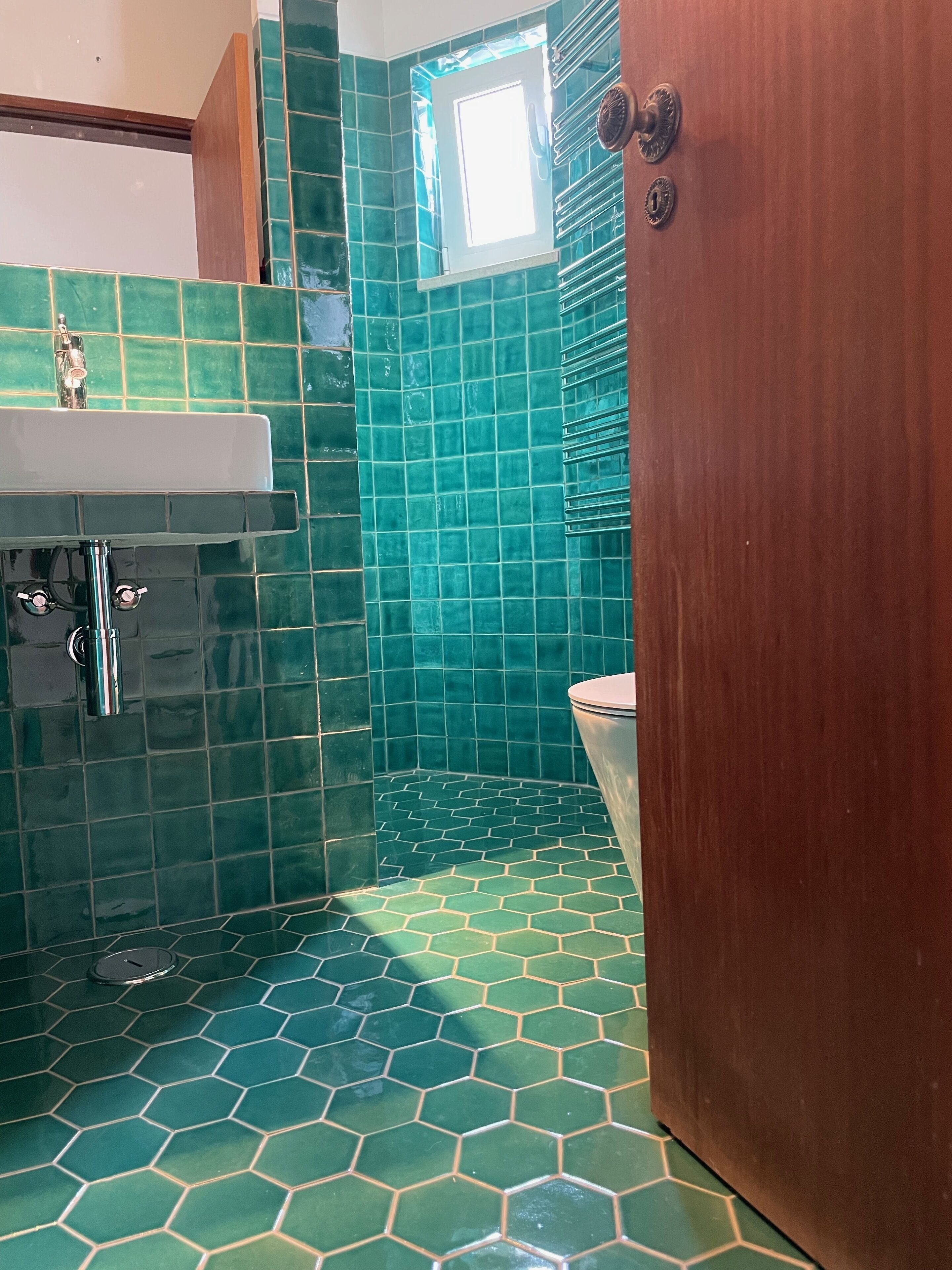 Une salle de bain avec des carreaux hexagonaux verts, un lavabo blanc et une porte en bois.