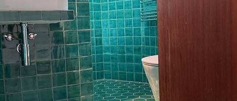 Une salle de bain avec des carreaux hexagonaux verts, un lavabo blanc et une porte en bois.