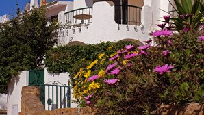 A white building with a yellow-striped umbrella, stone wall, and pink flowers. - Cozy Apartment with Stunning Sea Views, One Minute Walk from the Beach (Praia da Luz, Lagos)