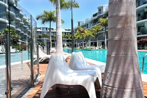 A poolside area with lounge chairs, a palm tree, and a modern building with balconies. - LIGHT AND DESIGN IN THE EXCLUSIVE AND RELAXED AREA OF EL PALMMAR, SOUTH TENERIFE (Arona)