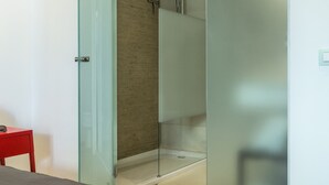 Un dormitorio moderno con cabina de ducha de vidrio, una silla roja y una cama con cubierta oscura.