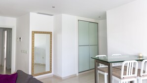 Una sala moderna con una mesa de comedor de vidrio, sillas blancas, un espejo grande y un armario con puerta corredera de cristal.