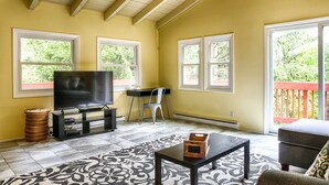 A living room with a TV, a desk, and a chair. There are large windows and a balcony with a red railing. - Country Escape! 5 bed/5bath, 2 acre pond, pool/Foosball tables, Fire pit, Sauna (Roxbury)