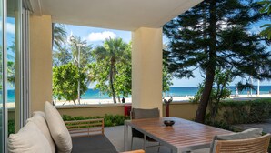 Ein Balkon mit Holztisch und Stühlen mit Blick auf einen Strand und das Meer.