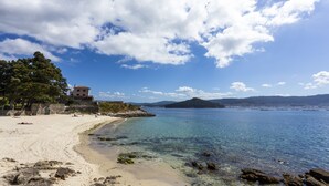A beach with clear water, a sandy shore, and a building in the background.