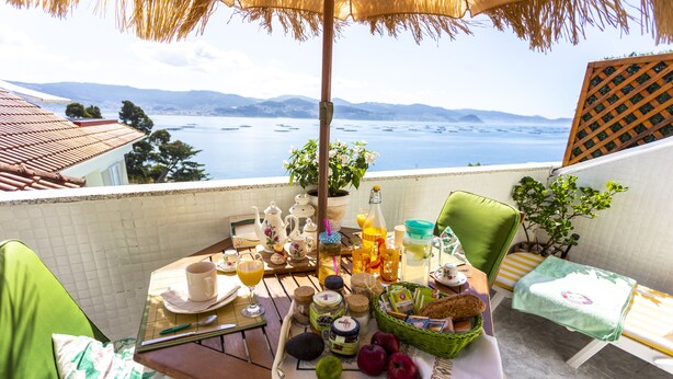 A balcony with a table set for breakfast, overlooking a scenic view of the sea and mountains.