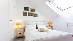 A bedroom with a bed, two bedside tables, a nightstand, a window, and wall art.