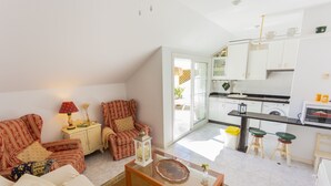 A cozy living room with a sofa, armchair, and coffee table, a kitchen with white cabinets and a dining area with stools.