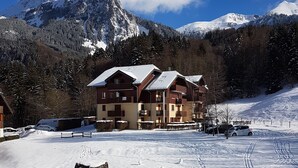Et snedækket skisportssted med en bygning i chalet-stil, skiløjper og et bjerglandskab i baggrunden.