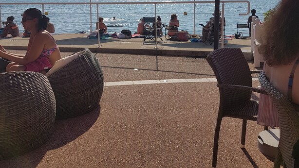 Et opholdsområde ved stranden med røde parasoller og fletstole med udsigt over havet.