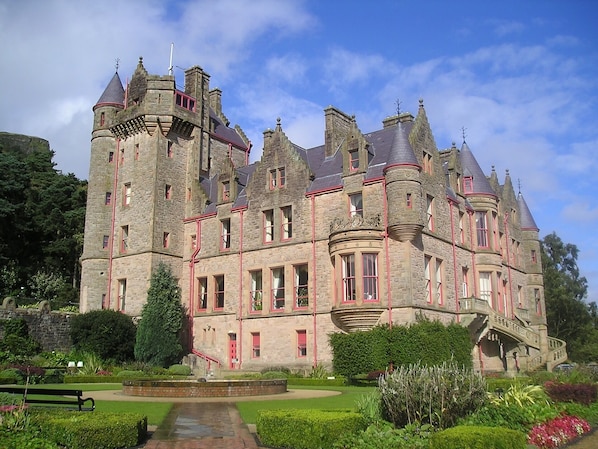 A large stone castle with multiple towers and turrets, surrounded by well-maintained gardens and a central courtyard.
