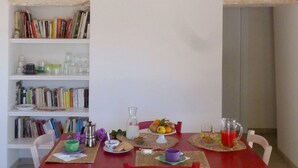 Ruokailutila, jossa on punainen pöytä, katettuna kahdelle, ja jonka ympärillä on kirjahyllyjä täynnä kirjoja.