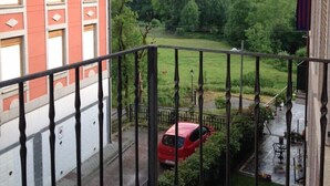 Un balcon d’où l’on peut admirer une voiture rouge garée dans une allée, entourée de verdure et avec une montagne en arrière-plan.