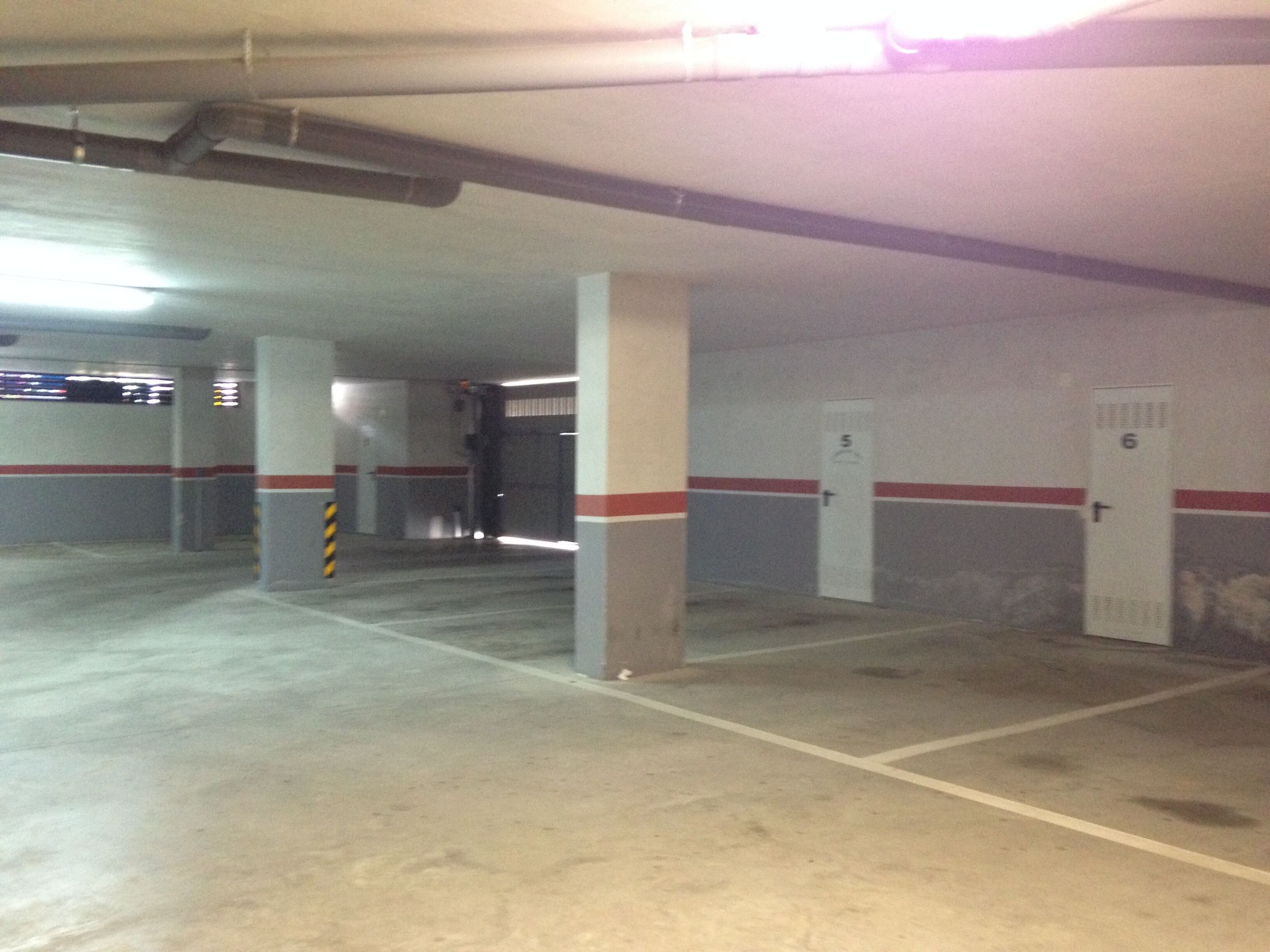 A multi-level parking garage with concrete pillars, white walls, and red stripes.