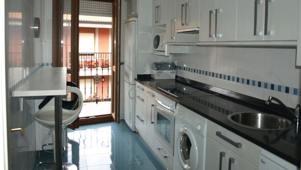Une cuisine de taille réduite avec des meubles blancs, un lave-linge et un évier.