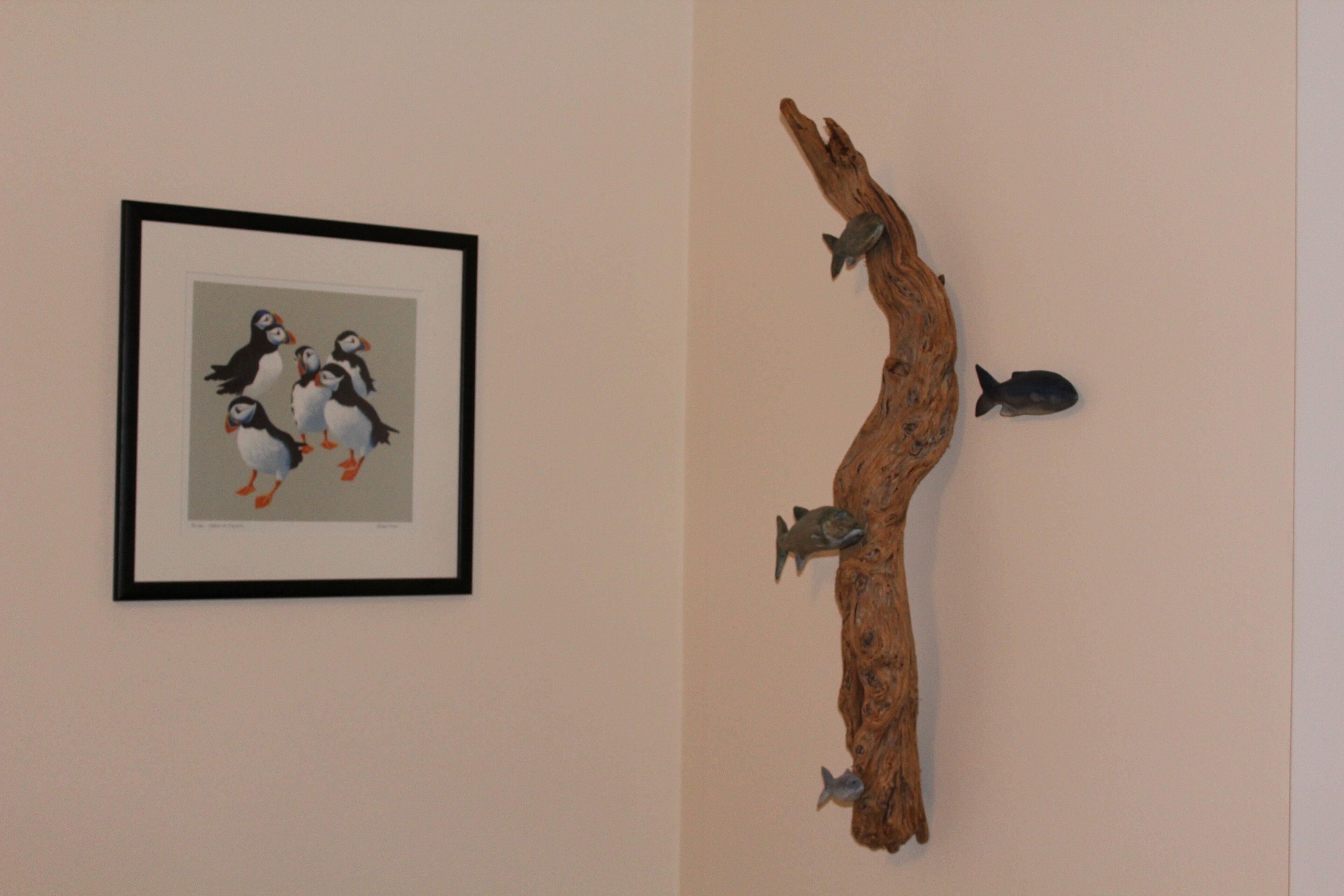 A framed artwork of penguins and a wooden sculpture with fish.