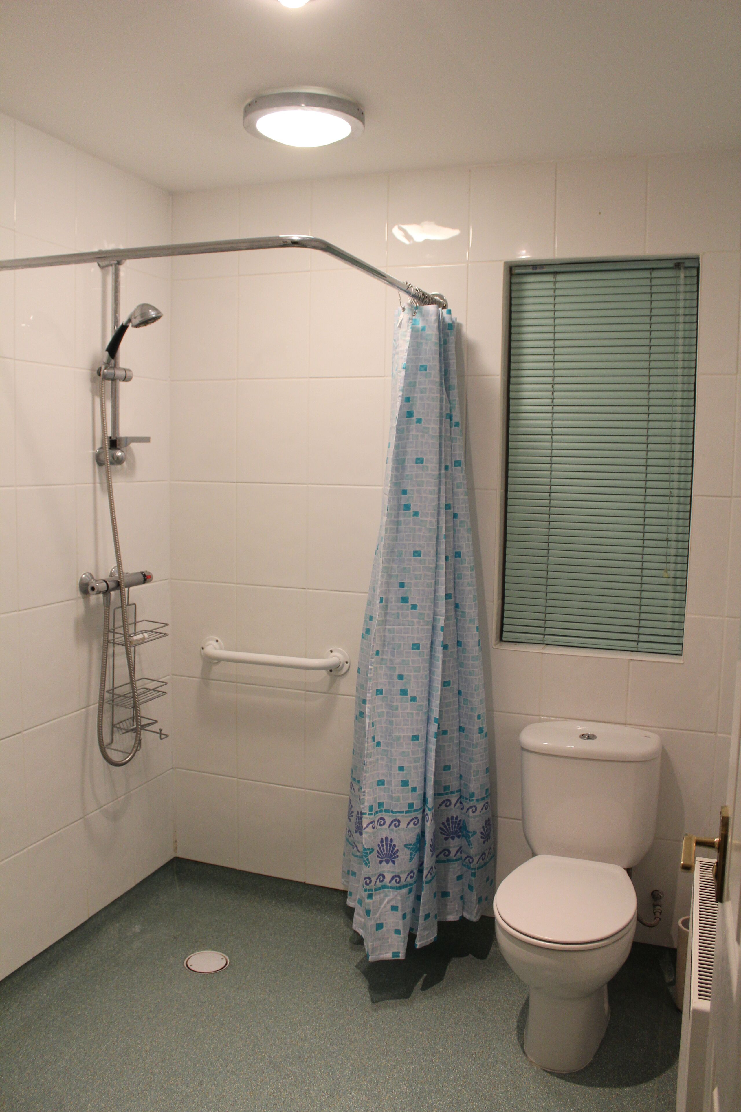 Une petite salle de bain avec une douche, des toilettes et une fenêtre équipée de stores.