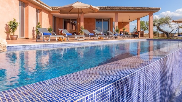 A swimming pool with tiled edges, lounge chairs, and a covered patio area.