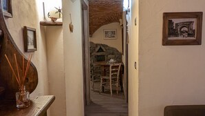A narrow hallway with a brick ceiling, leading to a dining area with a stone wall and a table.