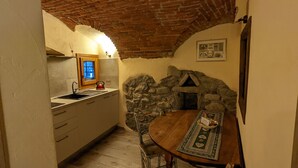 A rustic kitchen with a stone wall, wooden table, and a window with a cat visible.