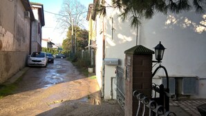 A narrow street with parked cars, a metal gate, and a building with a brick wall and a street lamp.