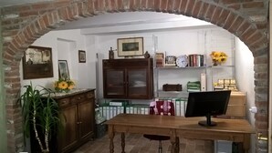 A room with a wooden table, a desk with a computer, a bookshelf with books and a clock, and a brick archway.