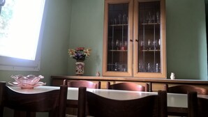 A dining area with a wooden table and chairs, a cabinet with glass doors, and a vase with flowers on the wall.