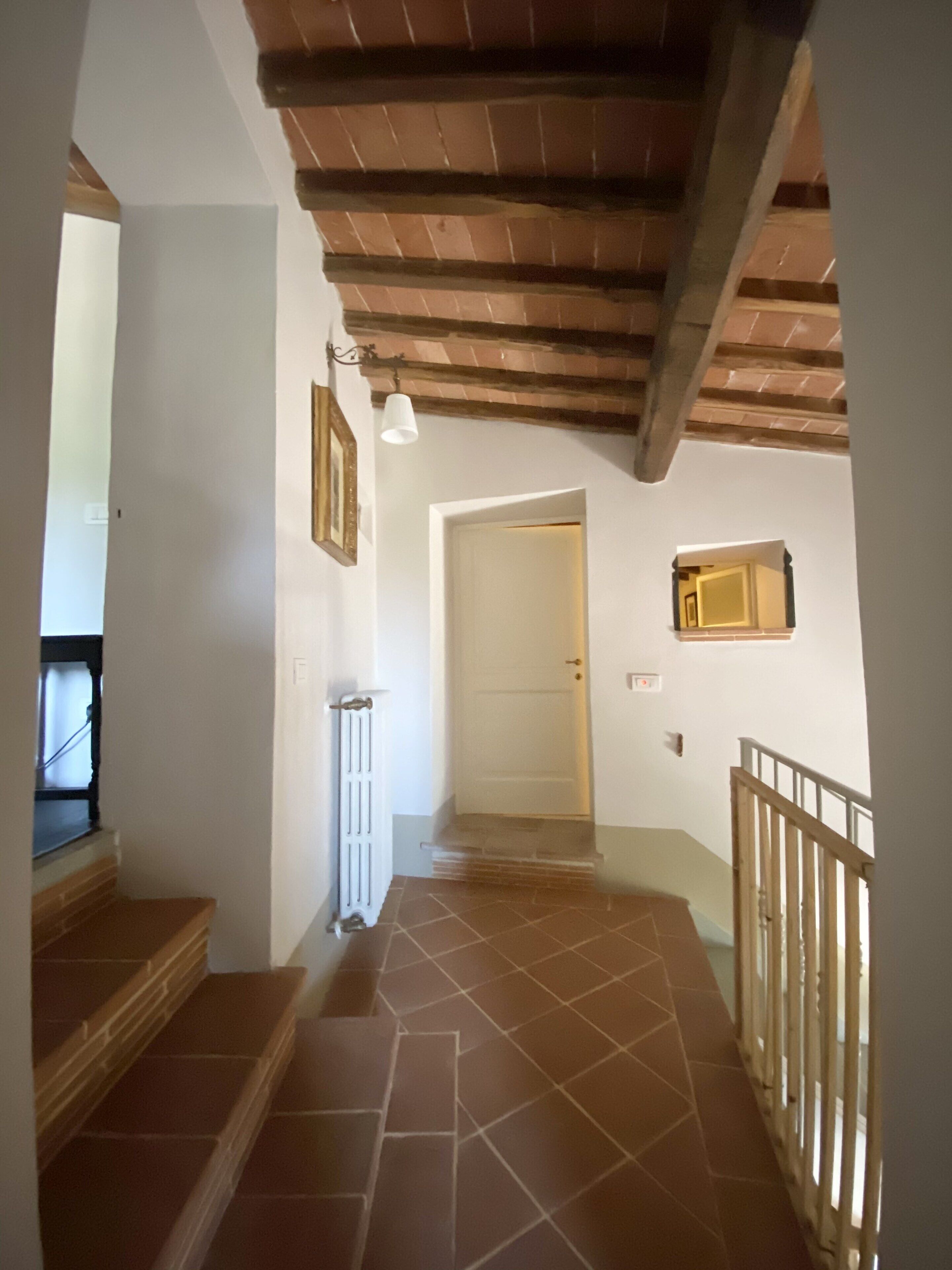 Una scala con gradini in legno che conduce a un pianerottolo, una porta bianca e una piccola finestra.