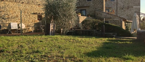 A stone building with a sloped roof, a small garden area with grass and a tree, and outdoor furniture.