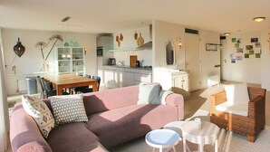 Ein modernes Wohnzimmer mit einem rosafarbenen Sofa, einem Esstisch und einer Küchenzeile.