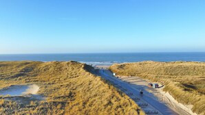 Ein Küstenpfad führt zum Strand, vorbei an Dünen, mit freiem Blick auf den Ozean.