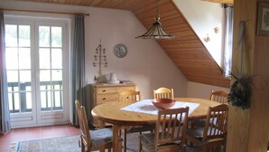 Un coin repas avec une table en bois, des chaises, un luminaire suspendu et une vue sur l’extérieur par une porte.
