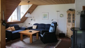 Un salon chaleureux avec un plafond en bois, un canapé, une table basse, un fauteuil en cuir noir, un meuble et une cheminée.