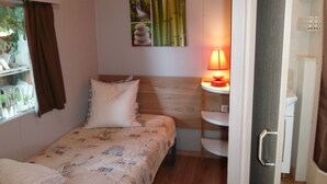 Een kleine slaapkamer met een bed, nachtkastje, lamp en een wandplank.