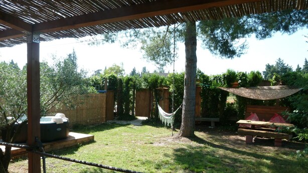 Een achtertuin met een houten pergola, een hangmat, een jacuzzi en een picknicktafel.