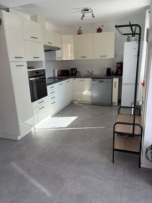 A modern kitchen with white cabinets, a built-in oven, a dishwasher, and a coffee maker.
