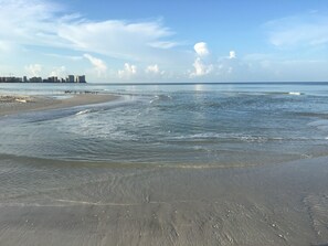A beach with calm waters, a sandy shore, and a distant city skyline.