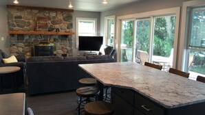 Una cocina moderna con una pared de acento de piedra, una isla grande con taburetes de bar, un televisor integrado y ventanas amplias que ofrecen vistas al exterior.