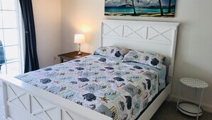A bedroom with a bed, a nightstand, a lamp, a painting, and a small table. - Ocean Pointe East - Go to outlets, bike to the beach! (Rehoboth Beach)