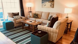 A living room with a sofa set, a coffee table, and two side tables with lamps. There is a striped rug on the floor. - Ocean Pointe East - Go to outlets, bike to the beach! (Rehoboth Beach)