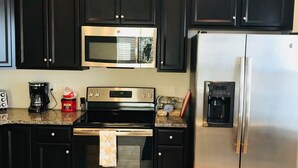 A kitchen with dark cabinets, a stainless steel refrigerator, a microwave, an oven, and a coffee maker. - Ocean Pointe East - Go to outlets, bike to the beach! (Rehoboth Beach)
