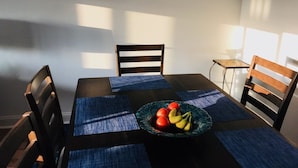 A dining area with a table set for four, blue placemats, a bowl of fruit, and two framed pictures on the wall. - Ocean Pointe East - Go to outlets, bike to the beach! (Rehoboth Beach)