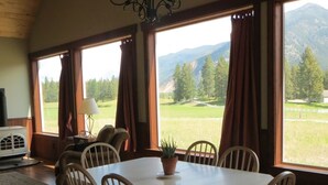 A dining area with a table and chairs, large windows with curtains, a chandelier, and a view of a mountainous landscape.