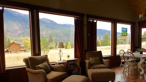 A room with large windows offering a view of a mountain landscape, wooden furniture, and a dining area with chairs and a table.