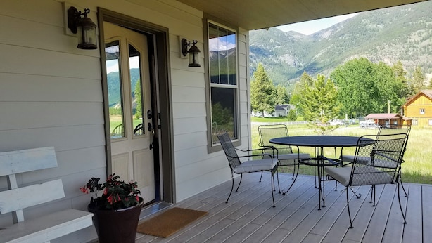 A covered porch with a table and chairs, a door with a view of mountains, and a potted plant.